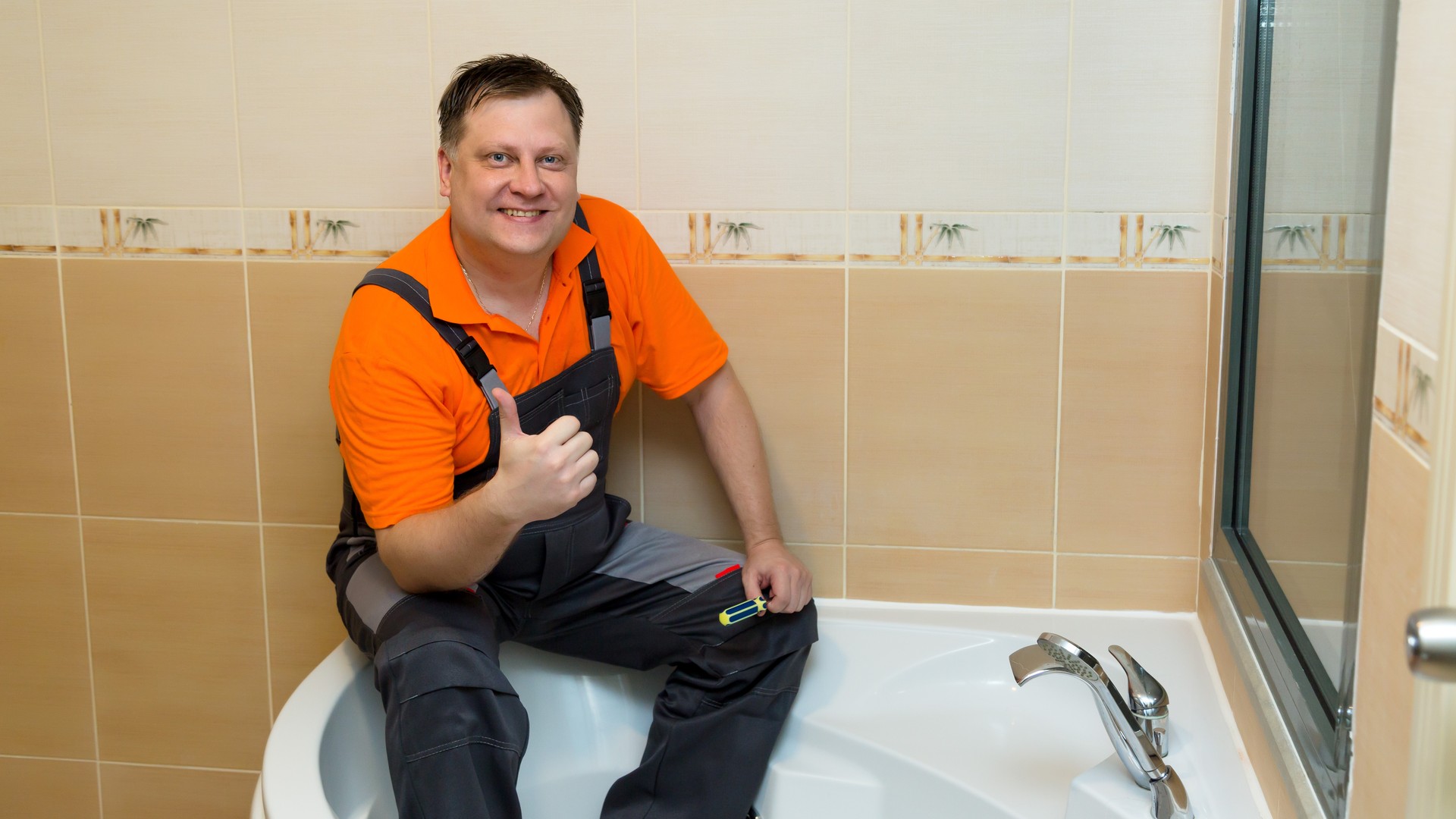 A man with a screwdriver sits on a large bathtub after renovation